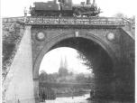 (11/12): Most kolejowy fot. n.n.<br>pocz. XX w. <br>Widok mostu kolejowego z 1862 r, W tle park miejski i bazylika katedralna. Na mocie lokomotywa.